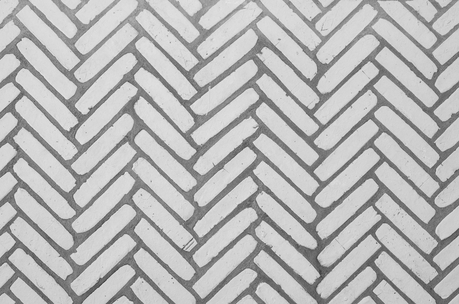 White pavers laid in a herringbone paver pattern with gray joints, each paver butting against the side of the next