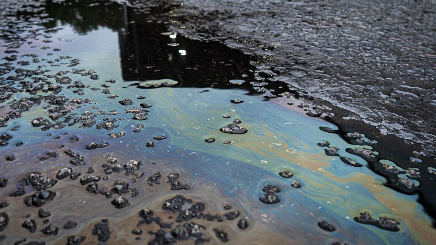 Fresh oil spill spreading across a paved surface, the kind of stain an oil and grease paver stain remover is made for