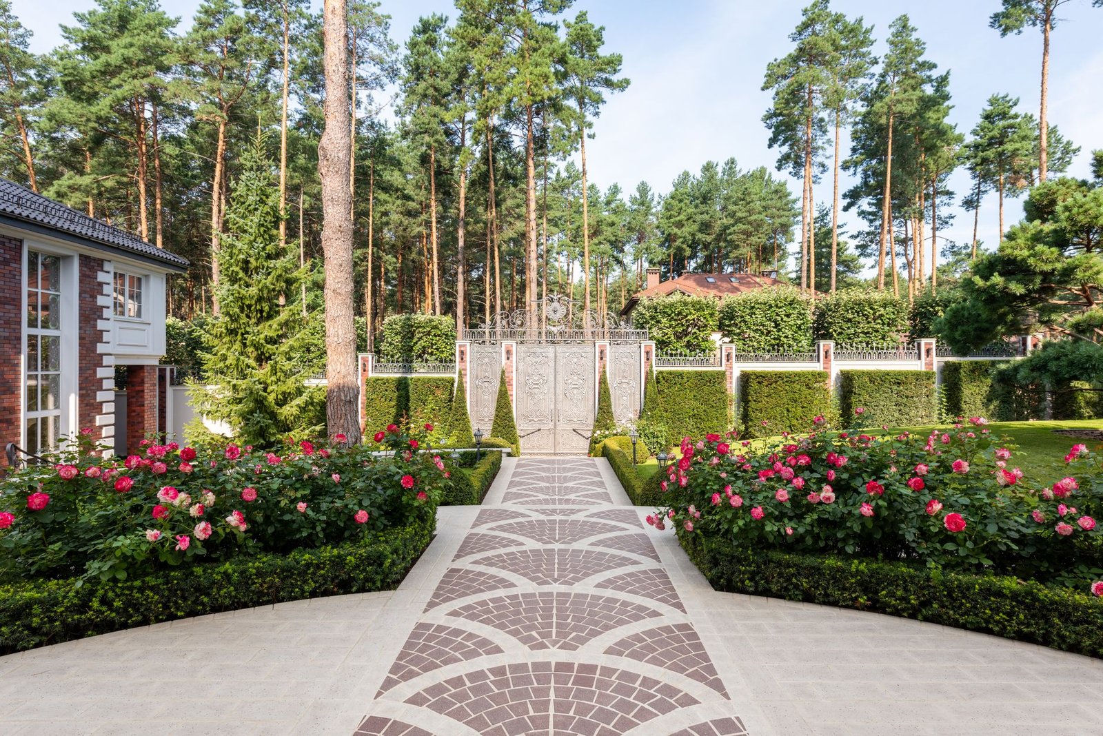 Garden walkway through rose beds with fan-shaped arcs of red pavers set into light gray paving, framed by borders on both edges