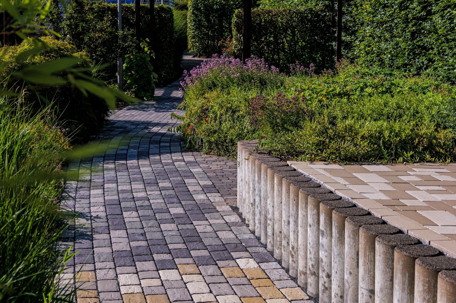 Curving gray and tan paver walkway with a soldier border winding between garden beds