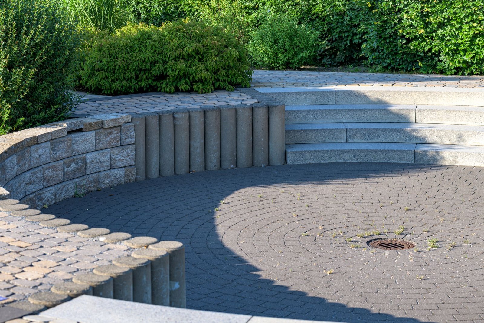 Gray concrete paver steps and curved retaining wall rising from a circular paver area