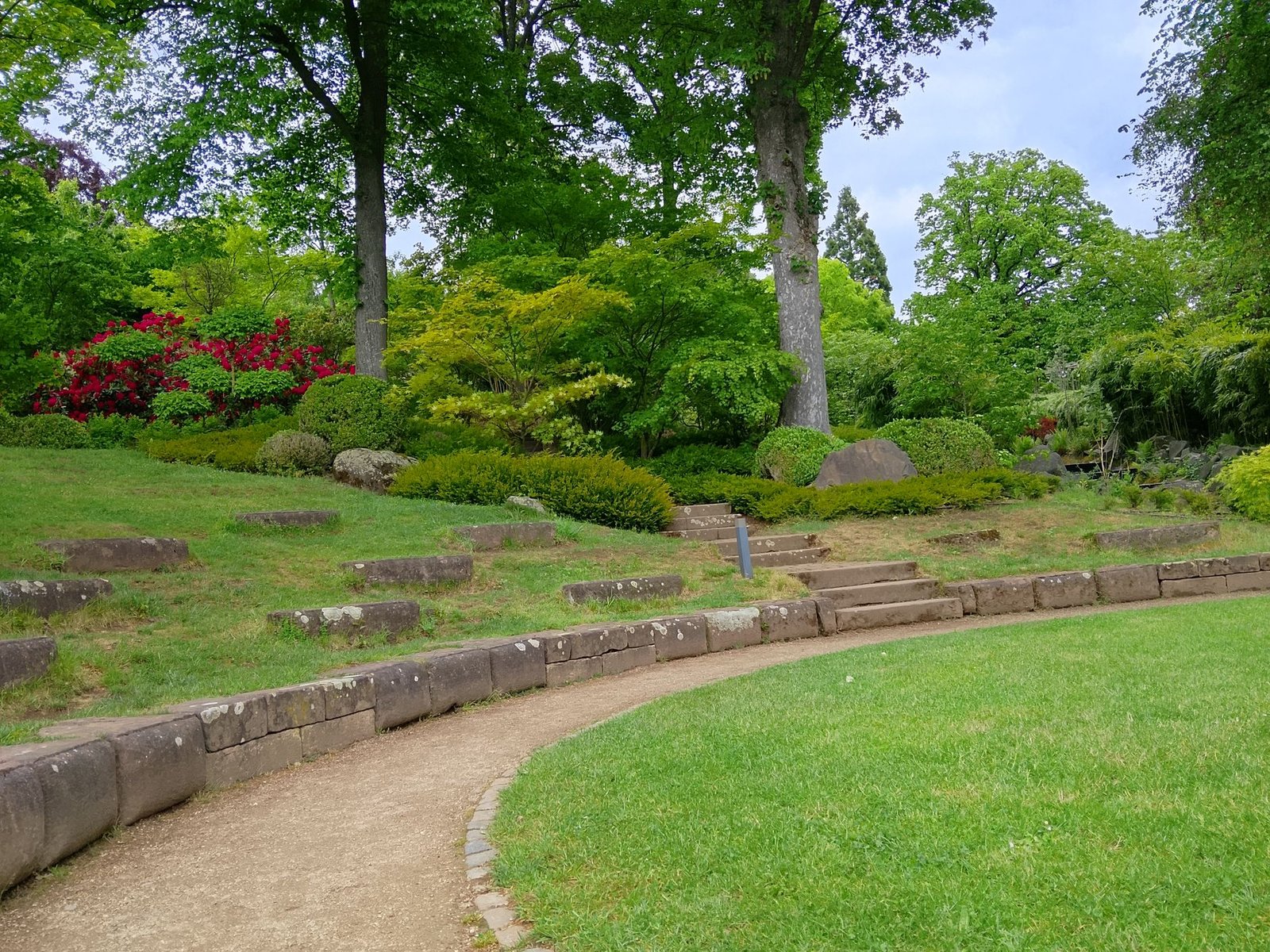 Curving gravel path held by a row of low stone curbs and a cobble edge beside a lawn