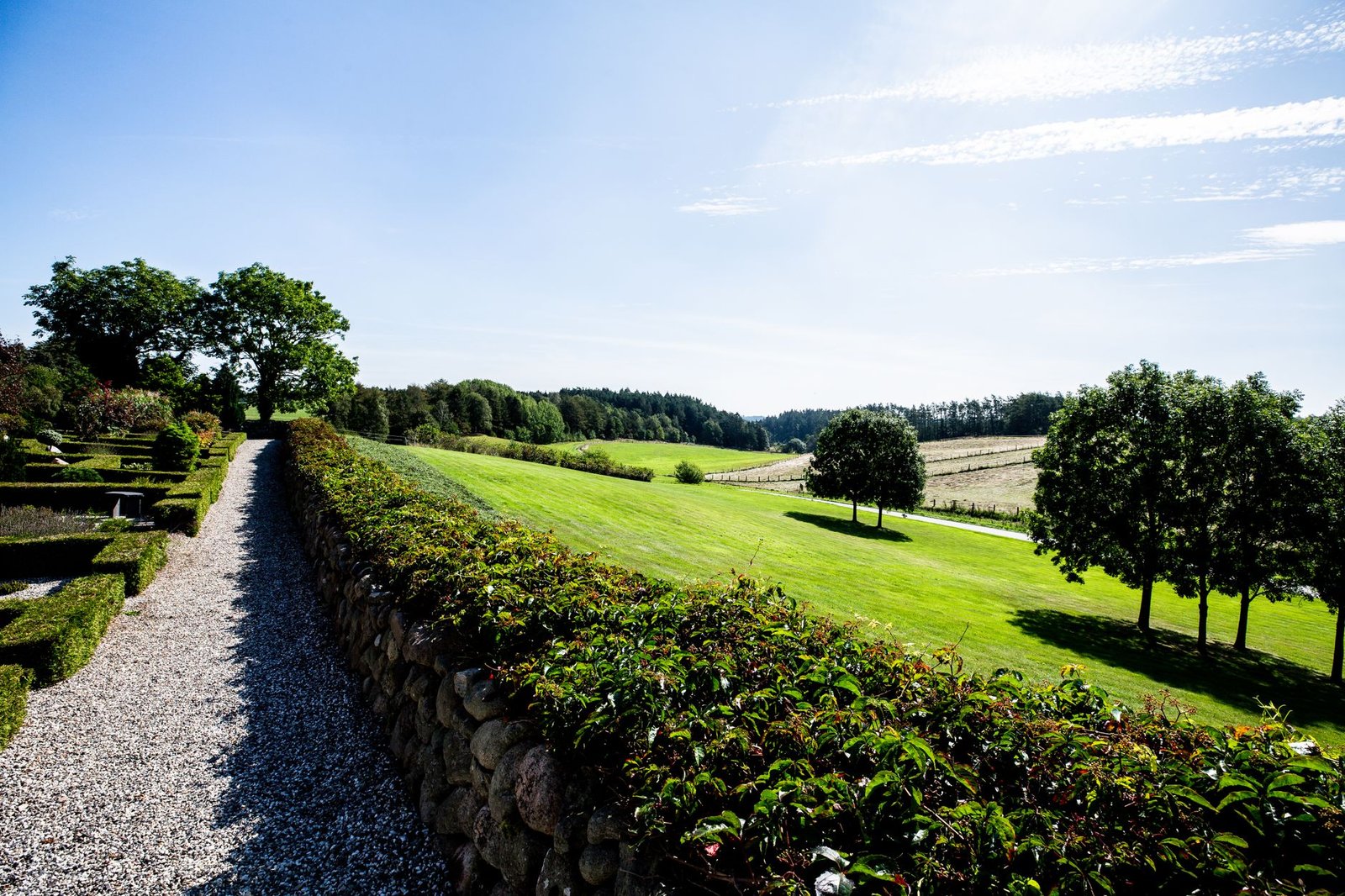 Long gravel garden path running beside a low stone wall topped with a hedge