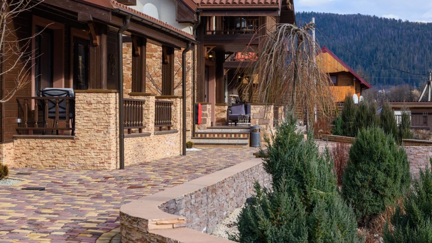 Paver terrace laid right up to a stone-clad house wall, with a downspout coming down onto the pavers
