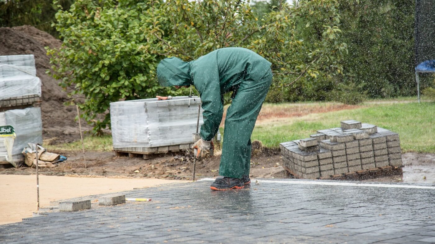 Installer setting gray concrete pavers on a flat prepared surface, the same laying work used for pavers over concrete