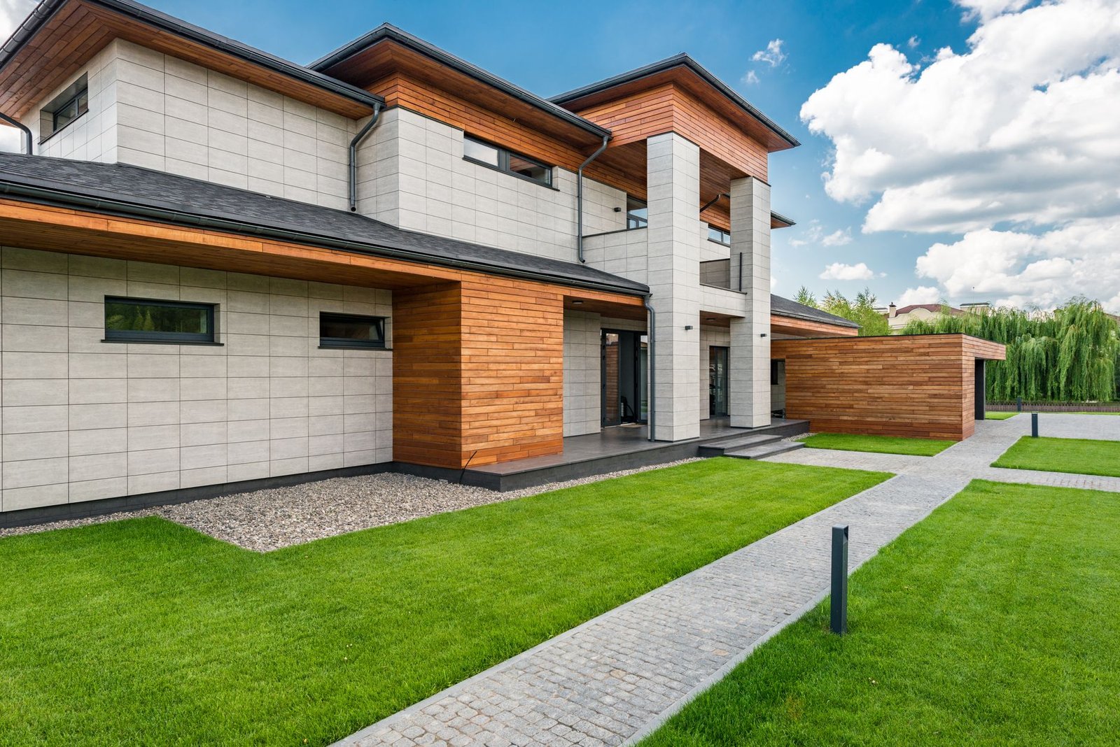 Modern house with a lawn and a straight walkway of gray concrete pavers leading along the side of the building