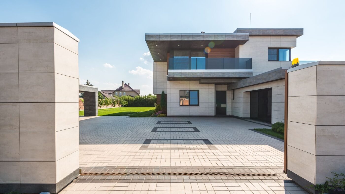 Modern house with a wide driveway and forecourt paved with gray concrete paving stones and darker accent bands