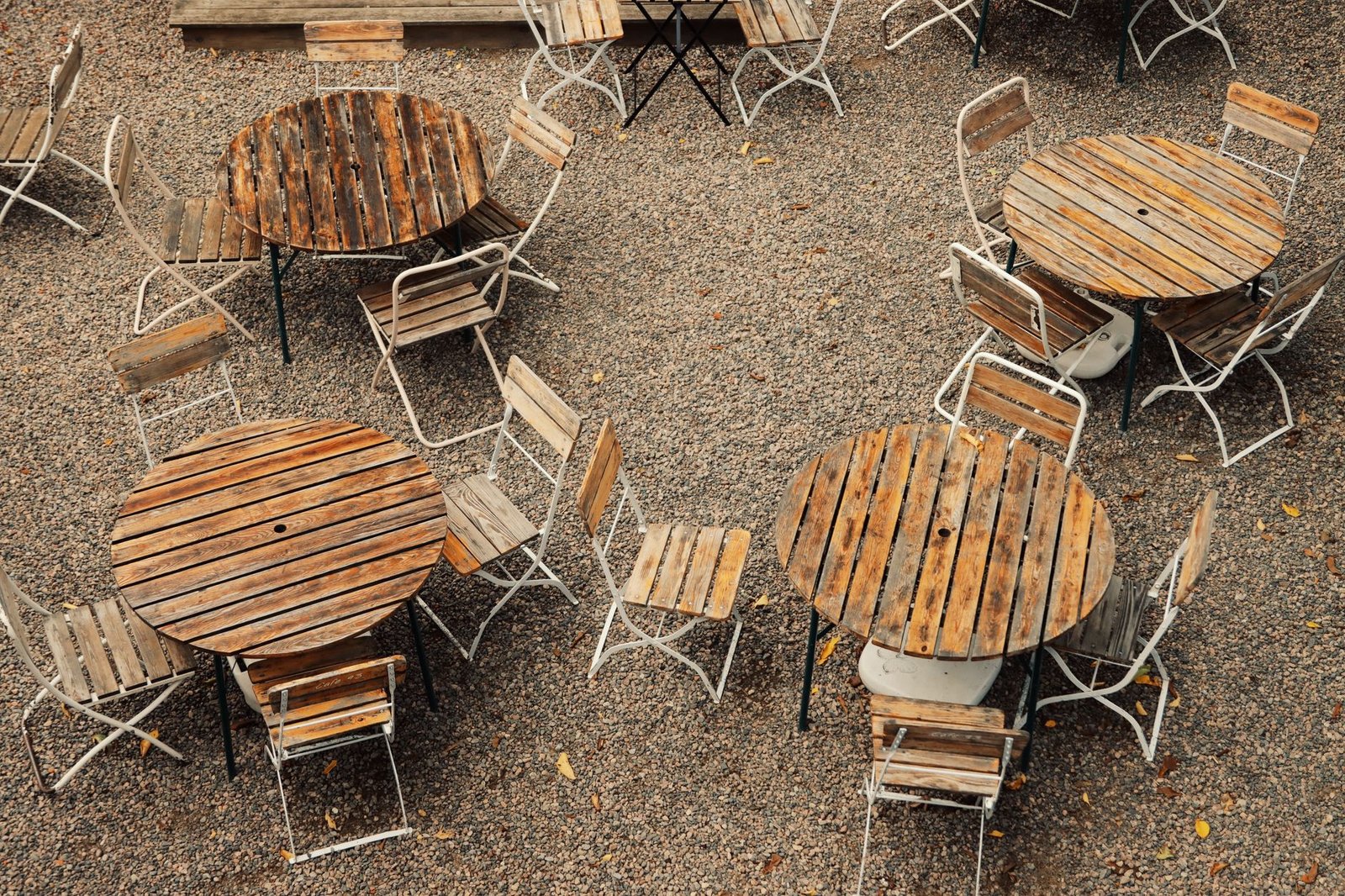 Wooden tables and folding chairs arranged on a loose gravel patio, seen from above