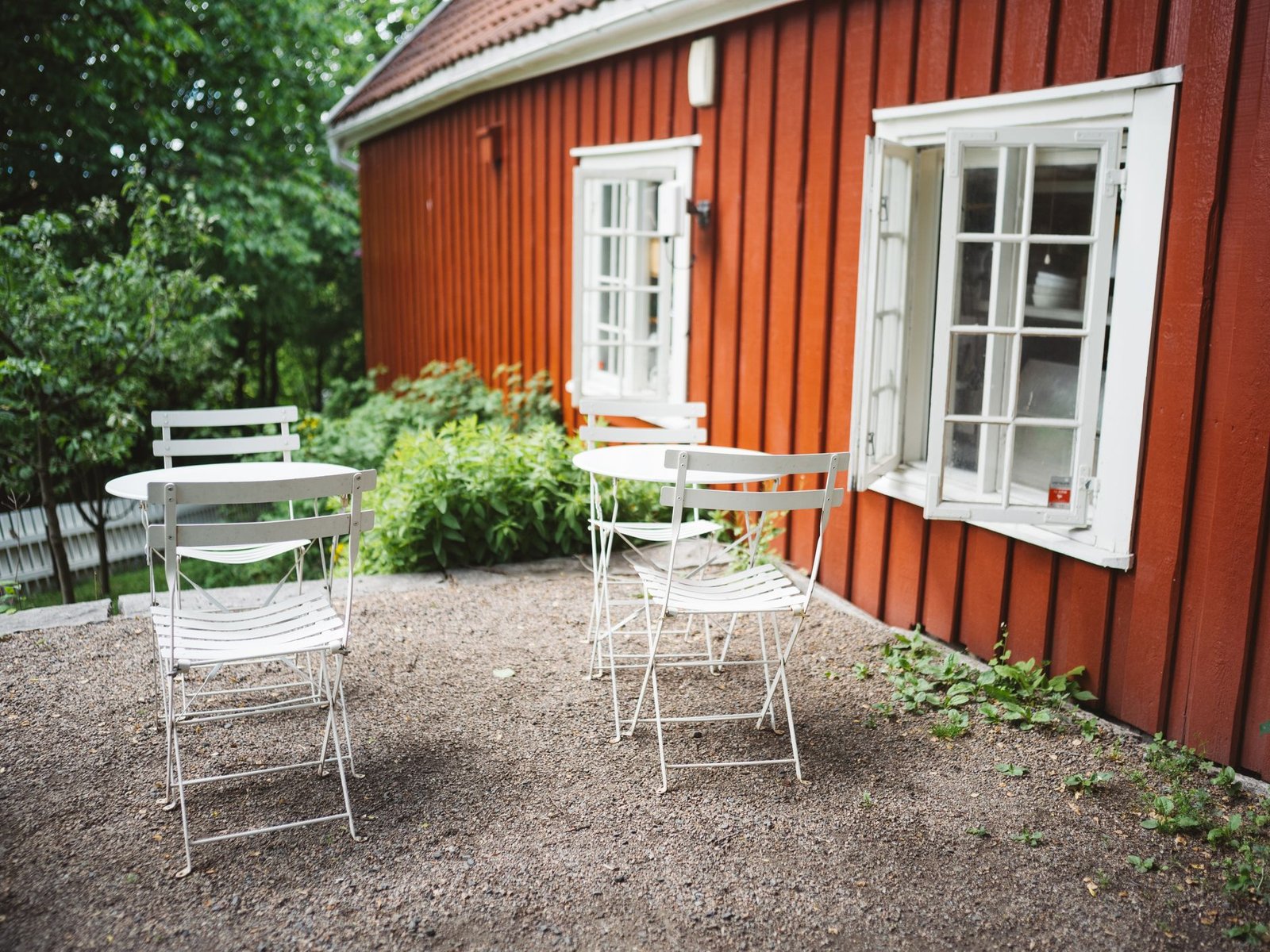 Gravel patio beside a red wooden house with white bistro chairs and tables on the raked stone