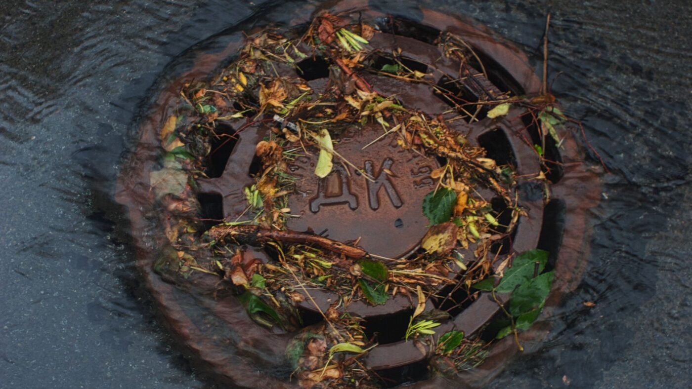 Stormwater and leaves rushing into a street storm drain, the runoff that permeable concrete pavers keep on site