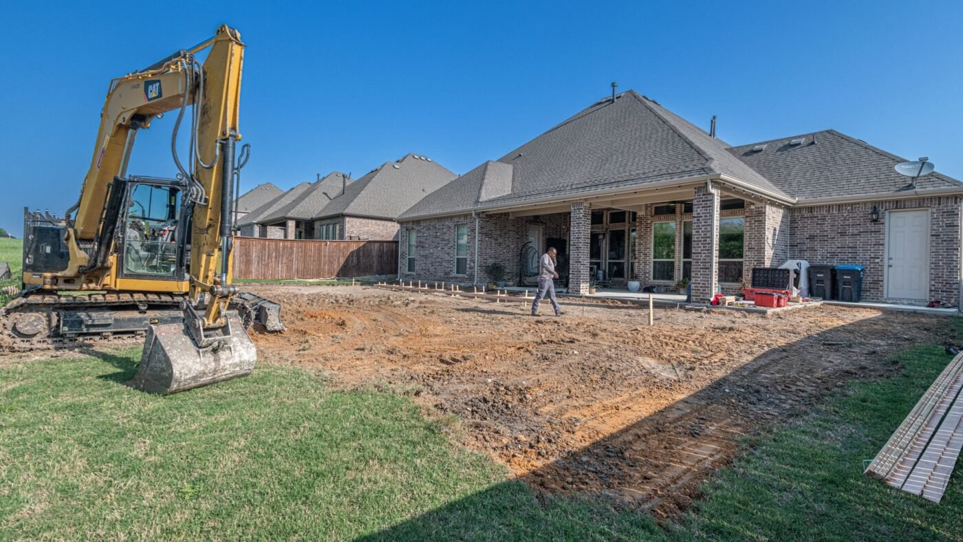 Backyard dug out for a new paver patio beside a brick house, the stage where a plate compactor rental is needed