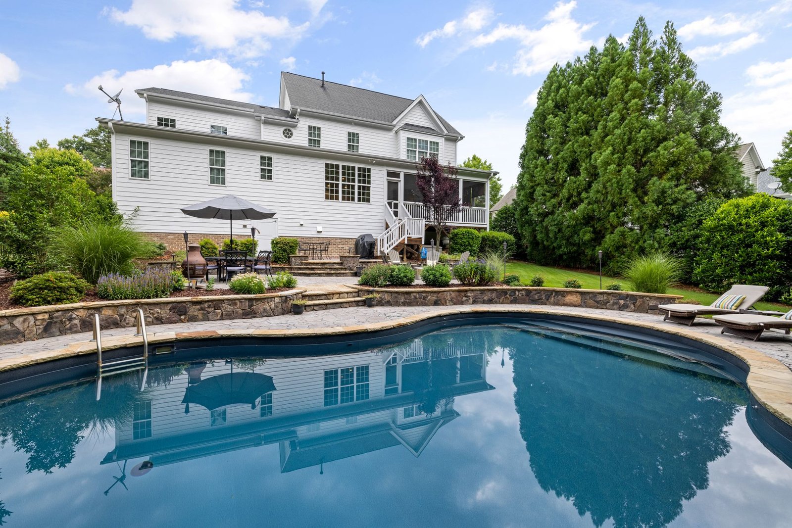 Freeform backyard swimming pool edged with natural stone coping and a stone patio behind it