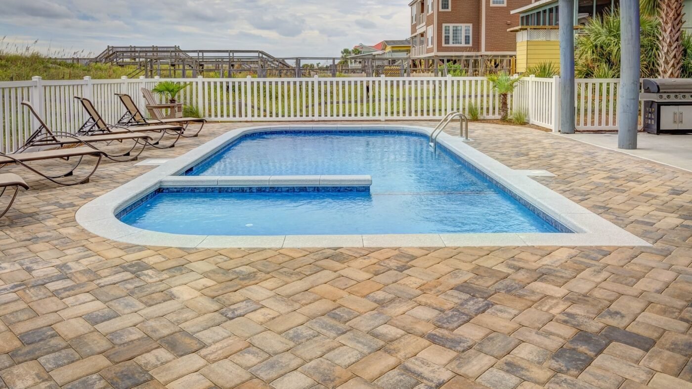 Backyard pool surrounded by a deck of tumbled concrete pavers in blended tan and gray, with rounded coping and sun loungers