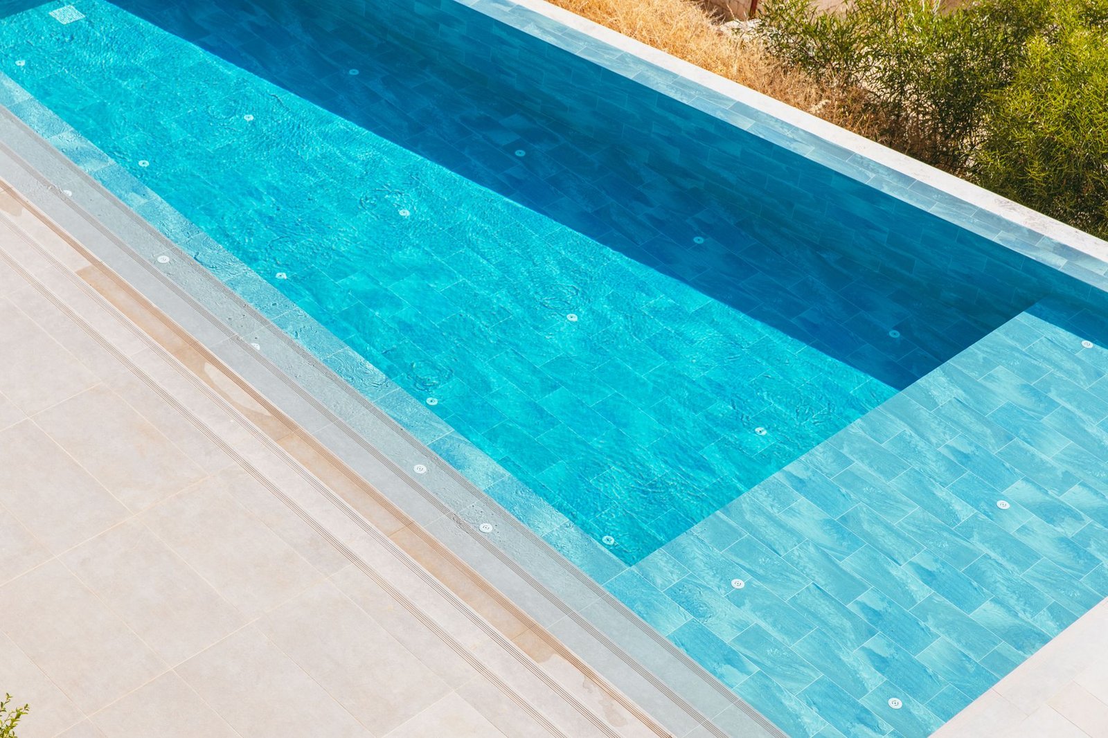 Pale large-format pool deck slabs beside a turquoise swimming pool with stepped coping