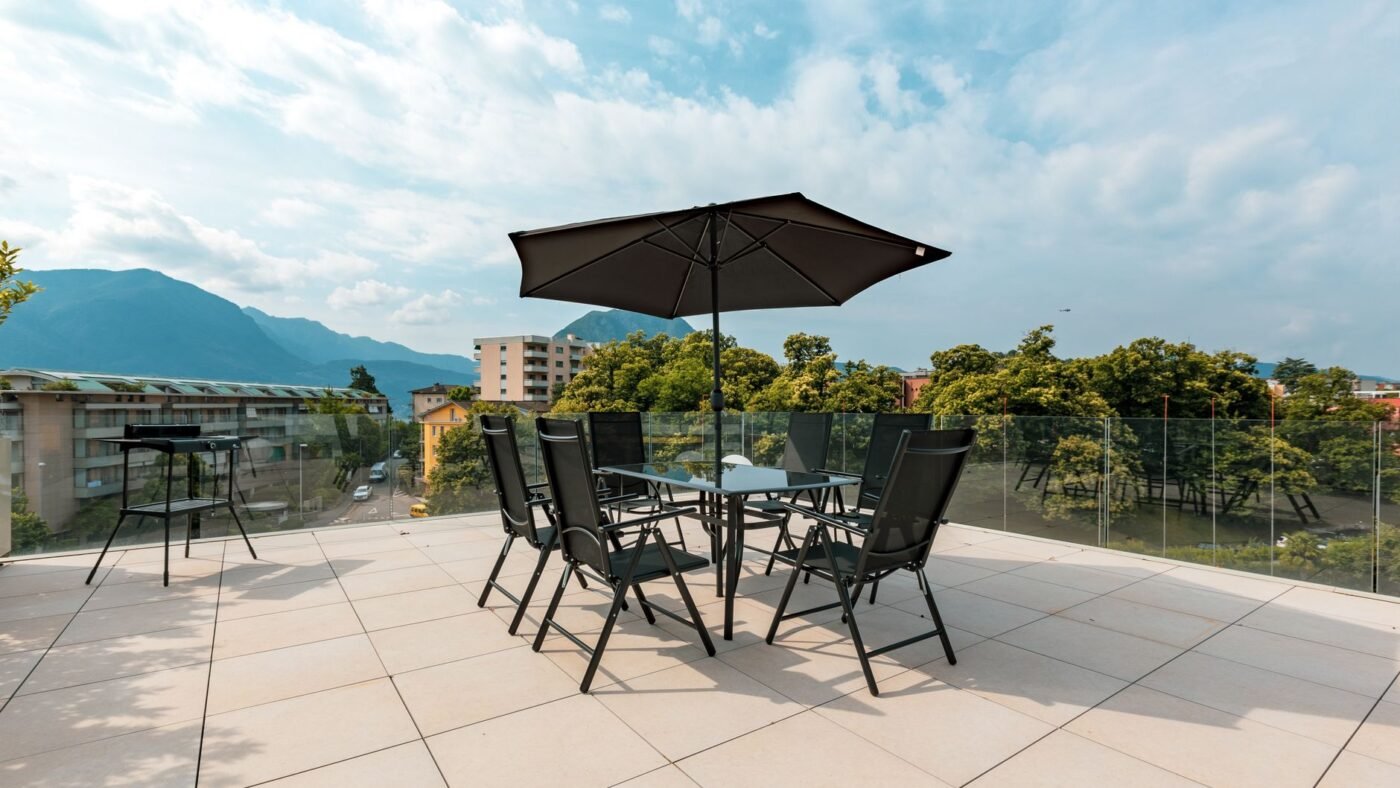 Large-format light porcelain-style tiles on a rooftop terrace with a glass railing, table and umbrella overlooking mountains