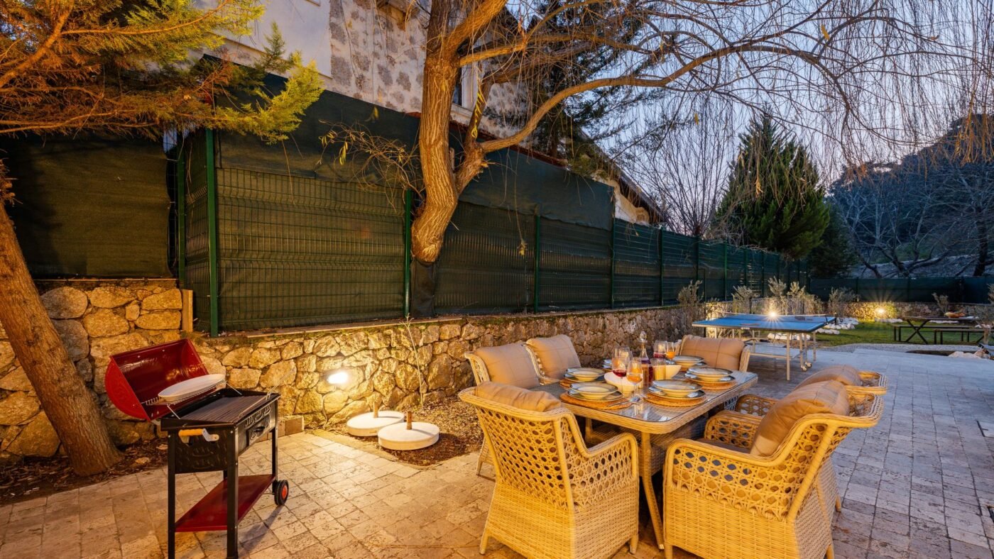 Paver patio with a dining table, wicker chairs and a charcoal grill at dusk, an area where grease and food spills make sealing pavers worthwhile