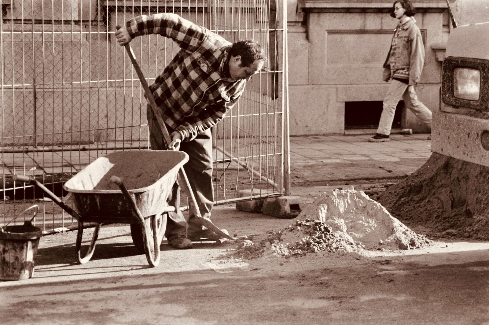 Worker shoveling a pile of sand into a wheelbarrow on a job site