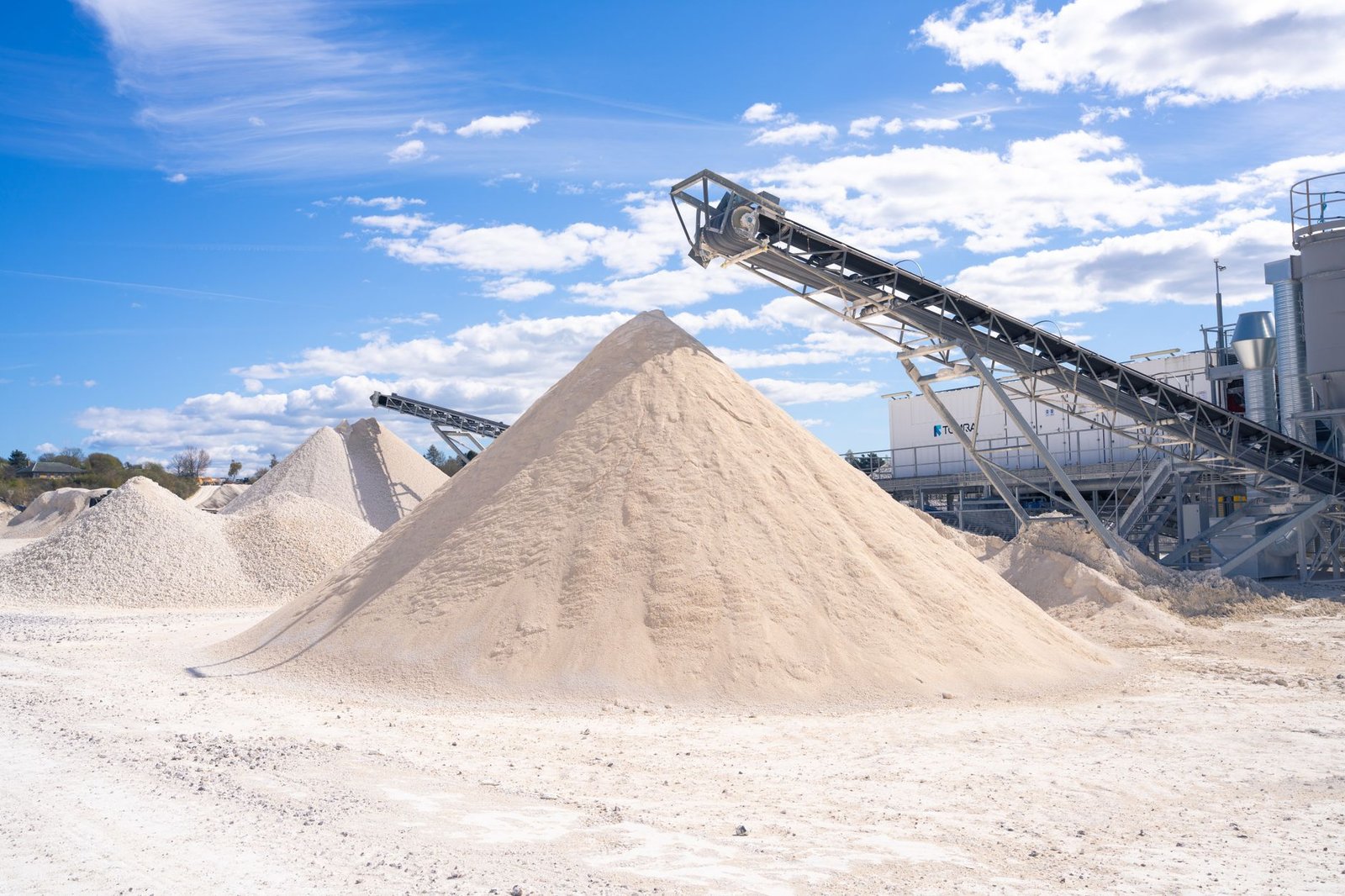 Tall stockpiles of washed sand at a sand and gravel yard with a conveyor, where screeding sand for pavers is bought in bulk