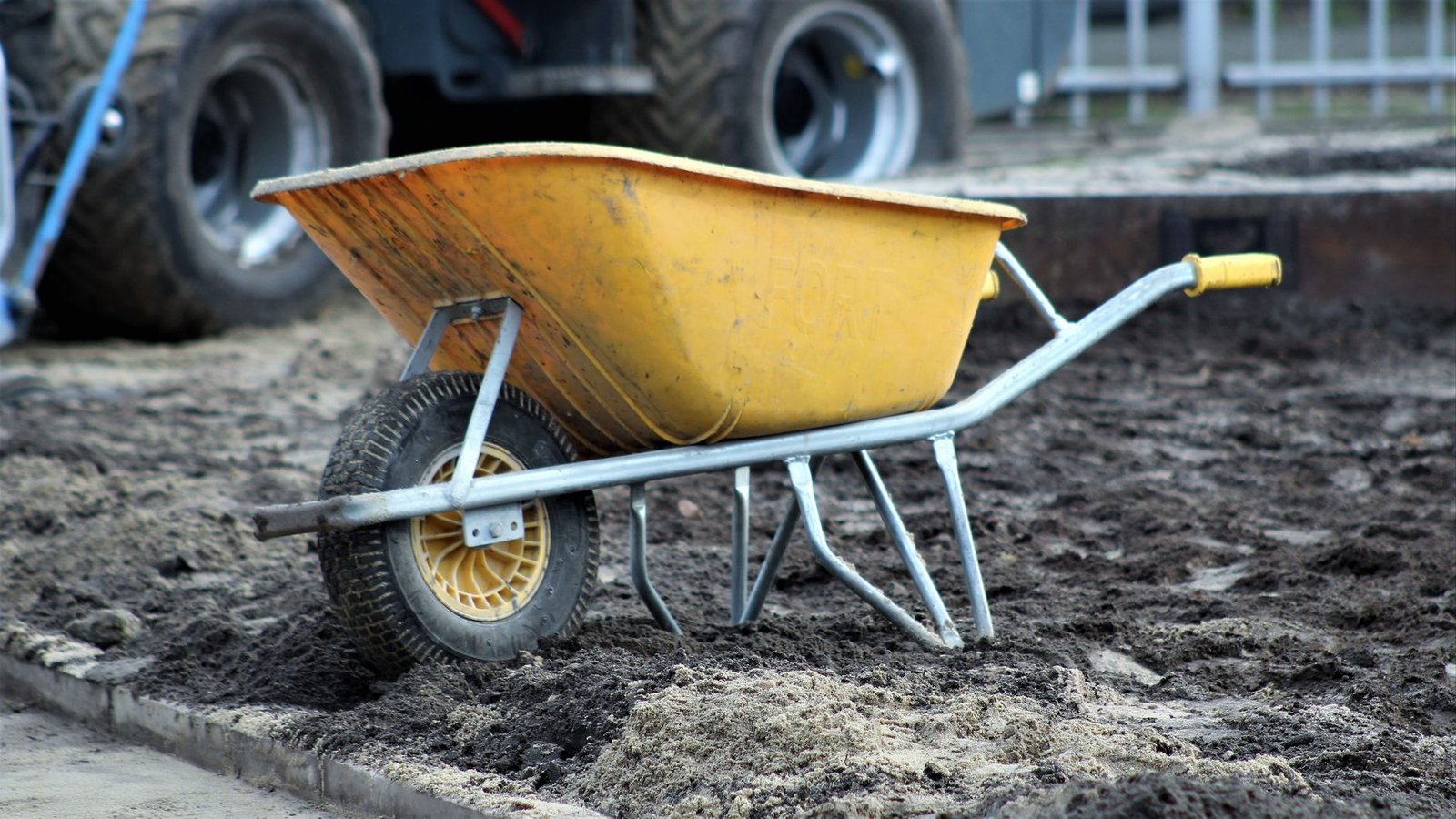 Yellow wheelbarrow on a job site beside loose sand and soil, ready to move bedding sand to the screed area