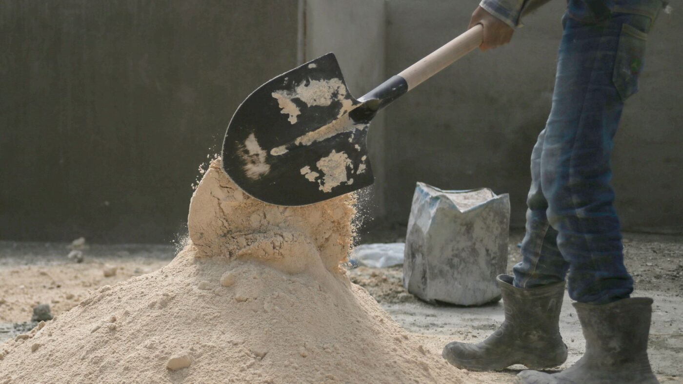 Shovel lifting damp coarse sand from a pile, the kind of bedding sand used for screeding under pavers