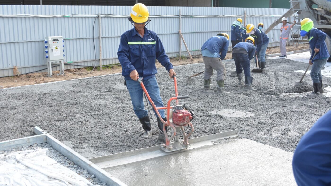 Construction crew leveling a freshly poured concrete slab with a vibrating screed, hours before control joints are sawn