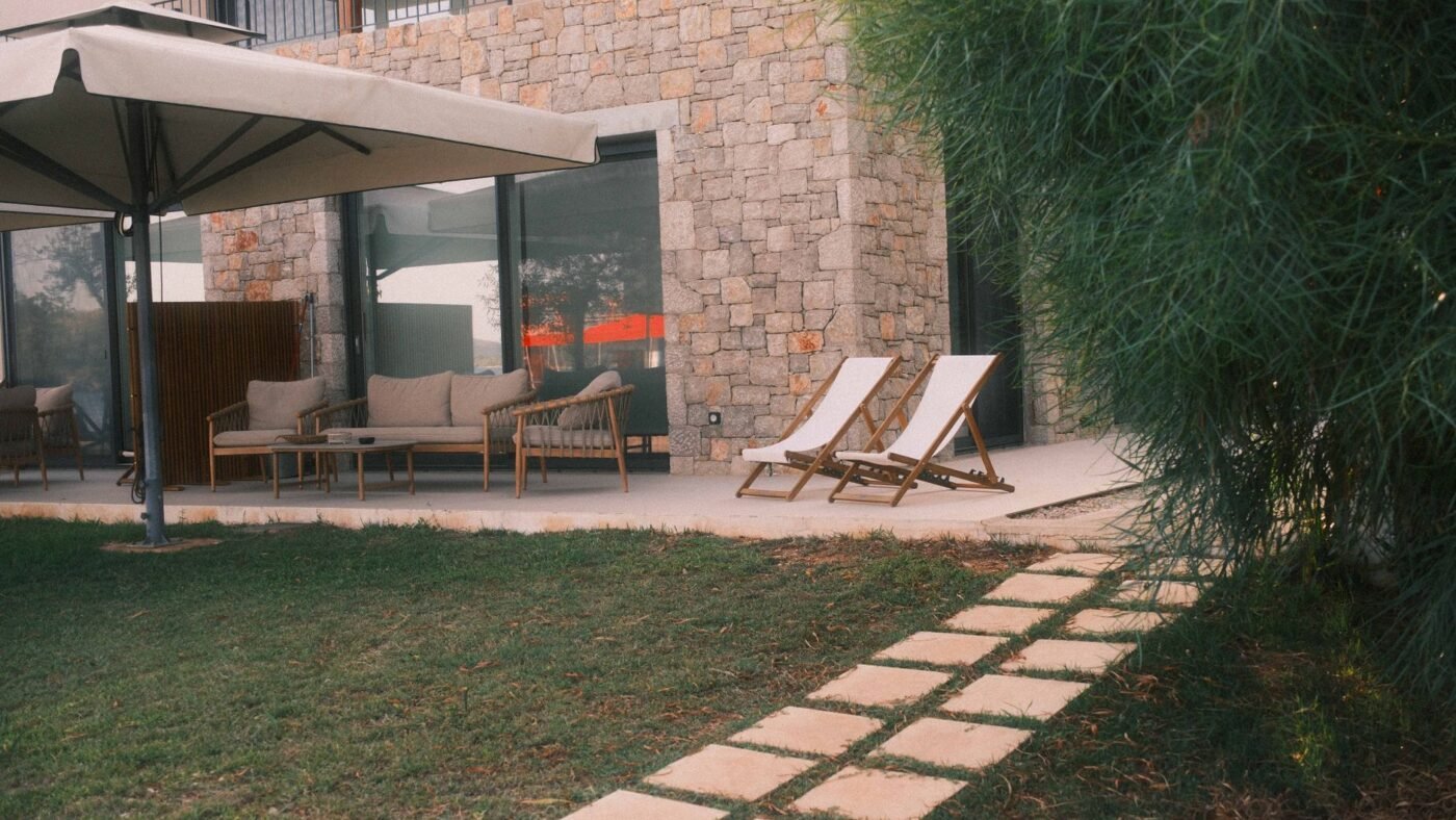 Backyard patio beside a stone house with a path of large rectangular concrete slabs set in the lawn