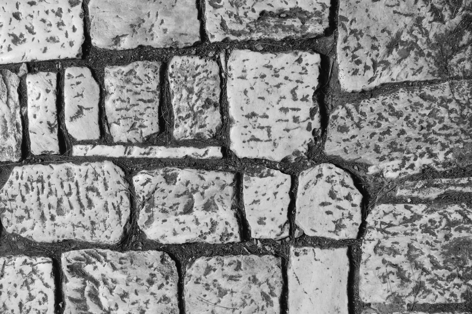 Close-up of worn stone pavers with rounded edges and dark joints of varying width between them
