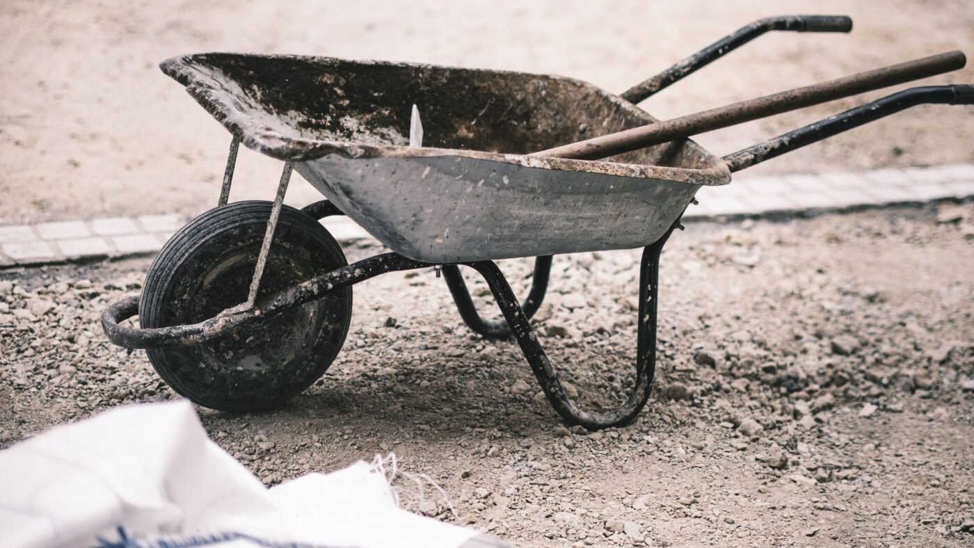 Wheelbarrow on a compacted gravel work area beside a paver edge, a small hardscape job where a hand tamper is used